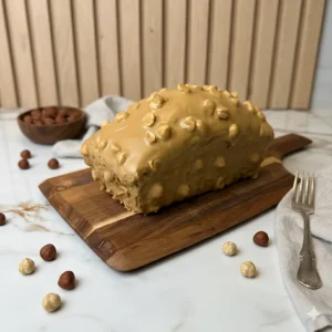 Cake noisette caramel avec ganache pochée et glaçage rocher noisettes, gâteau moelleux et gourmand posé sur une planche en bois.